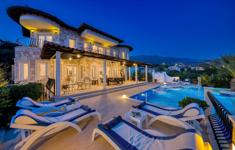 Luxury villa with a lit swimming pool and sun loungers at dusk