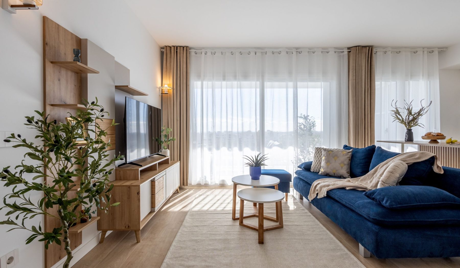 Panorama Valonia — Bright living room with blue sofa and Smart TV